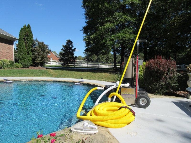 Pool Weasel system with hose coiled beside a pool near a horse fence